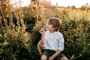 Young child in white shirt sitting among tall wildflowers at sunset.