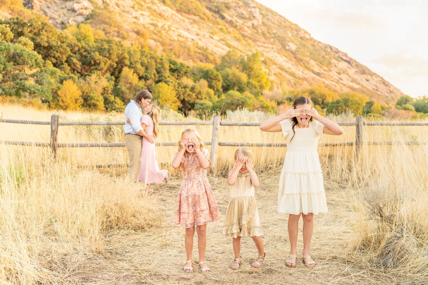 True to color photo of family dressed in pastel colors closing their eyes in front of their parents kissing at Hidden Valley Park.