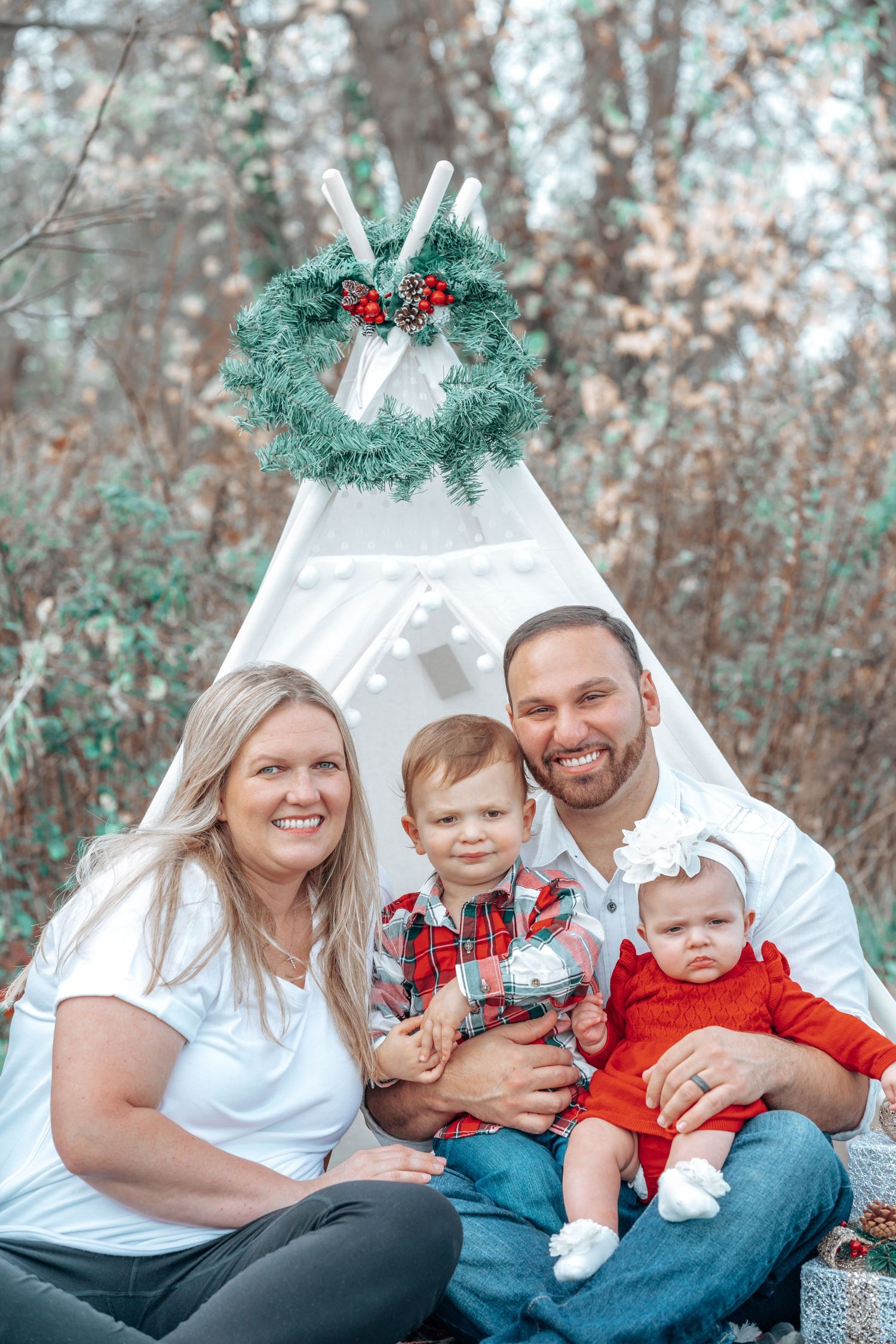 Winter family portrait in front of white teepee tent with holiday wreath and decorations.