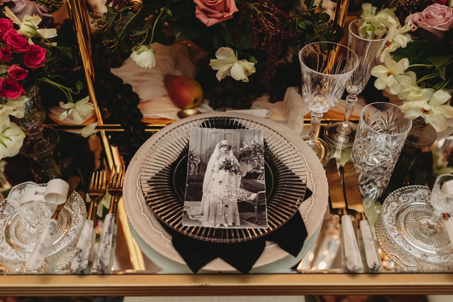 An elegant place setting with vintage plates, crystal glasses, and a black and white photograph.