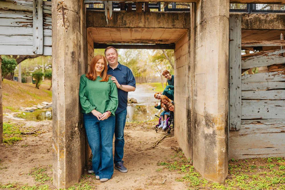 Family photo taken under rustic concrete archway with weathered wooden walls.