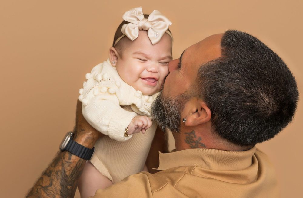 Tender moment captured between parent and baby in warm lighting against beige background.