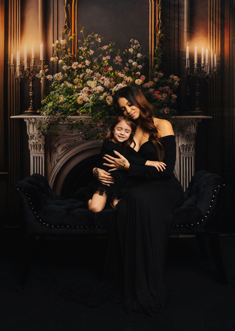 Intimate family portrait on black velvet couch with candlelit floral background.