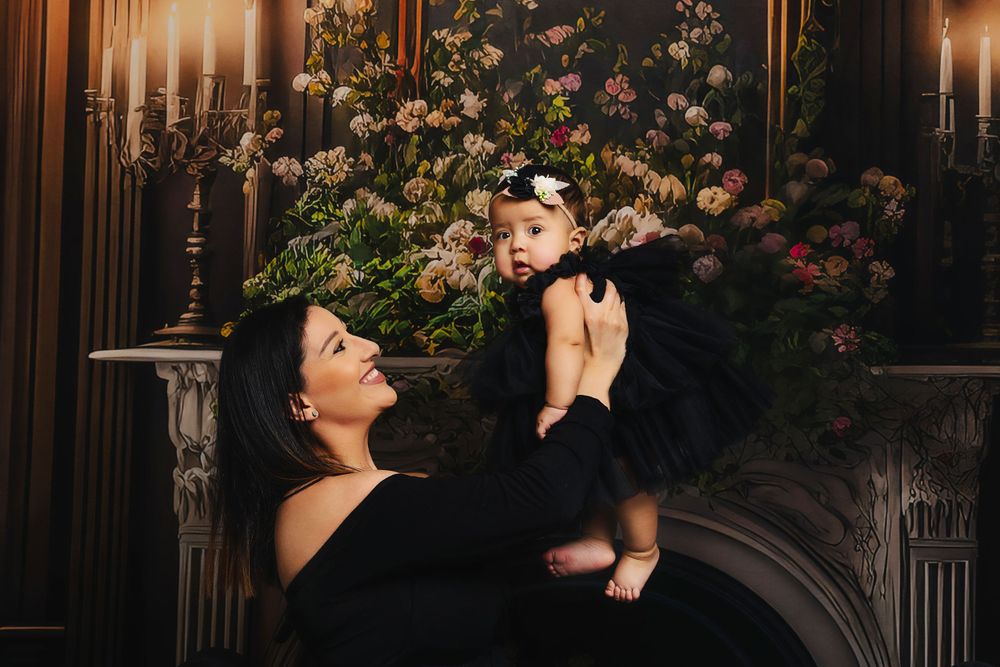 Elegant portrait by a floral-decorated fireplace with candles in dark, moody lighting.