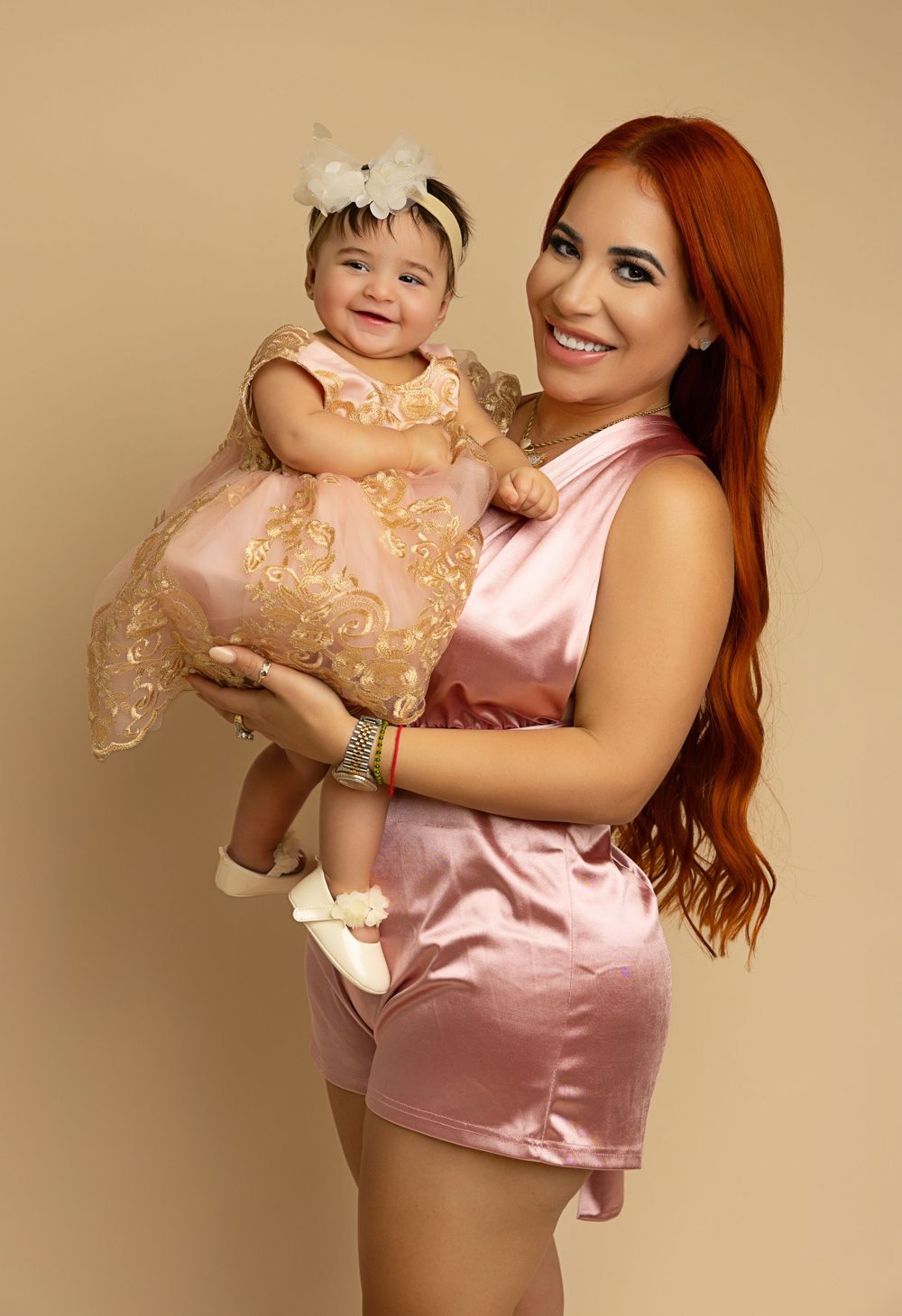Sweet portrait of a caregiver holding a baby in matching pink and gold outfits.