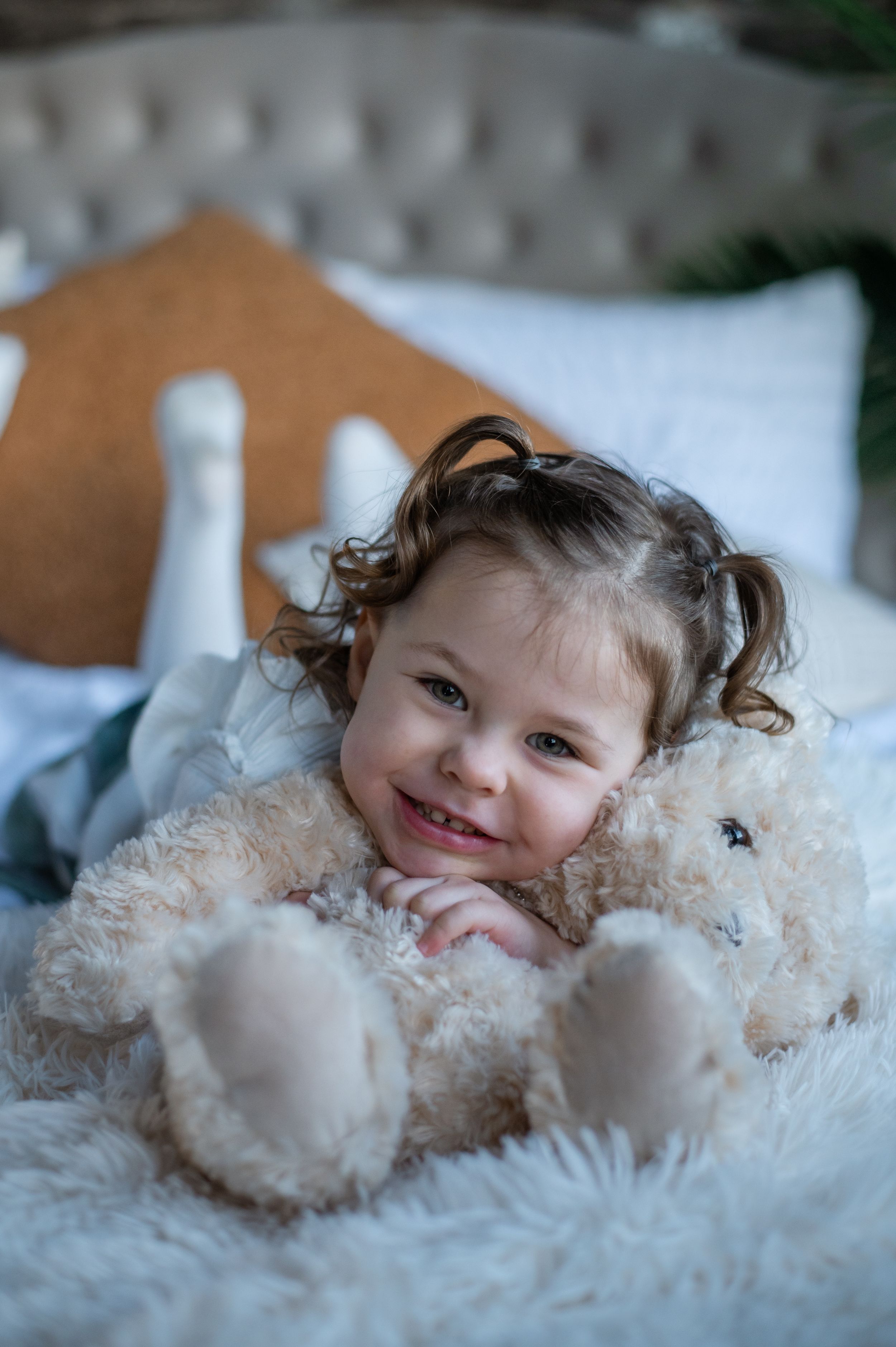 A toddler lying on plush bedding cuddling with a soft teddy bear.