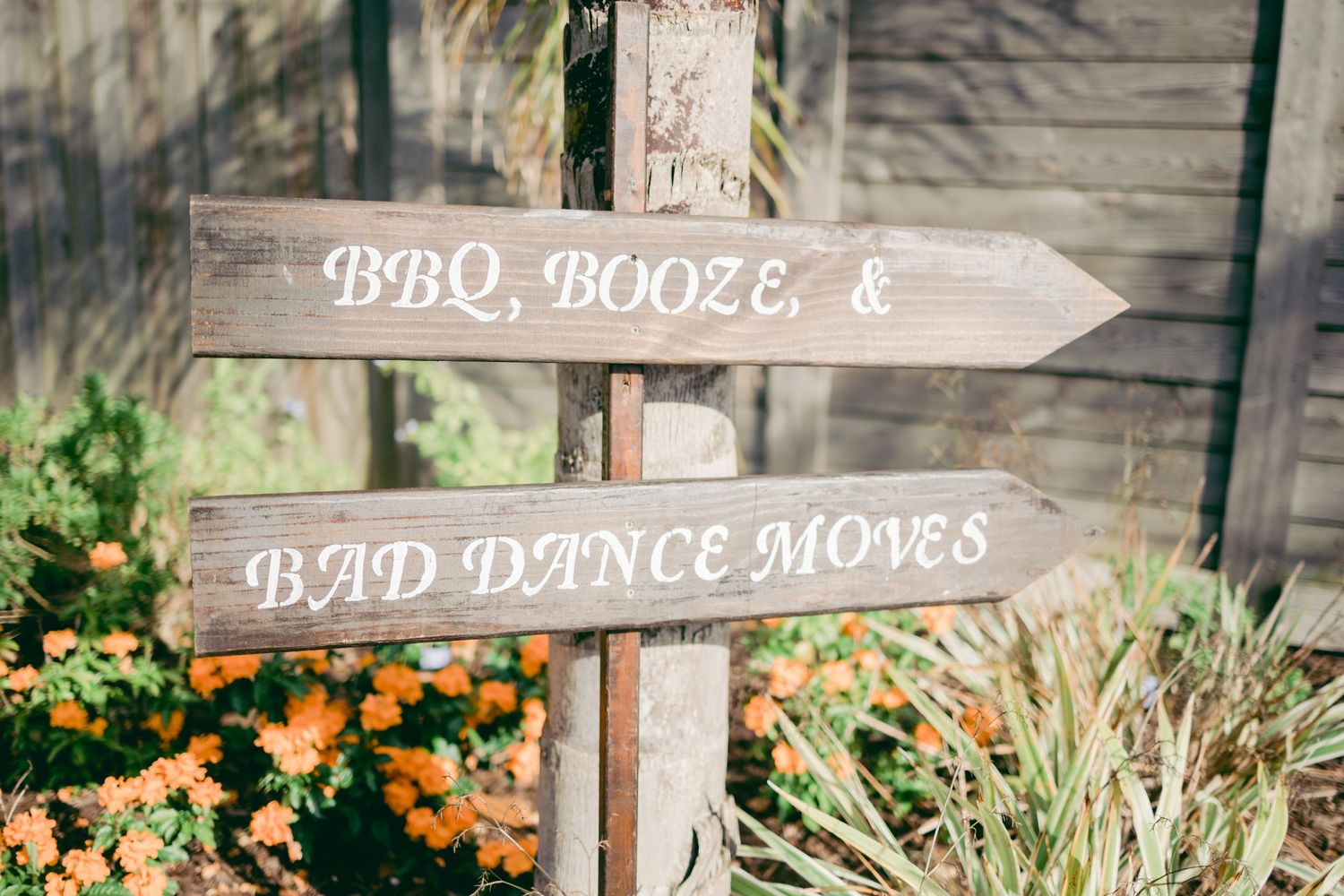 Wooden directional signs at a wedding venue pointing to BBQ, booze and dance areas.