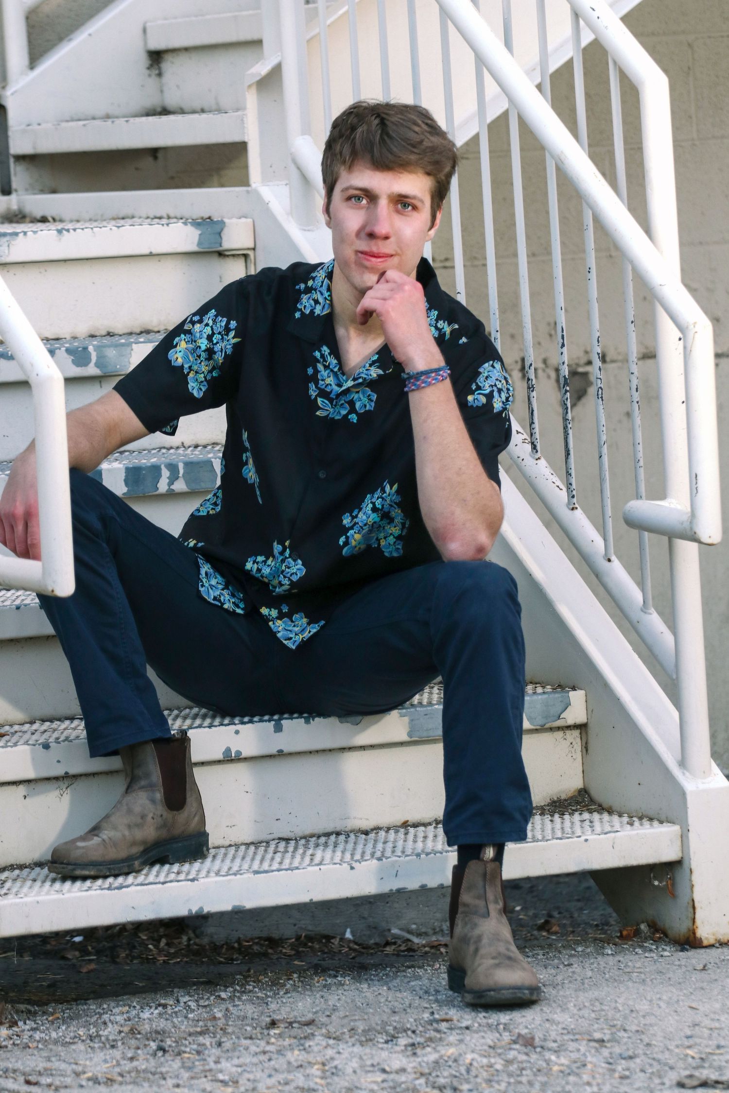 Person in floral shirt sits on white painted stairs in casual pose.