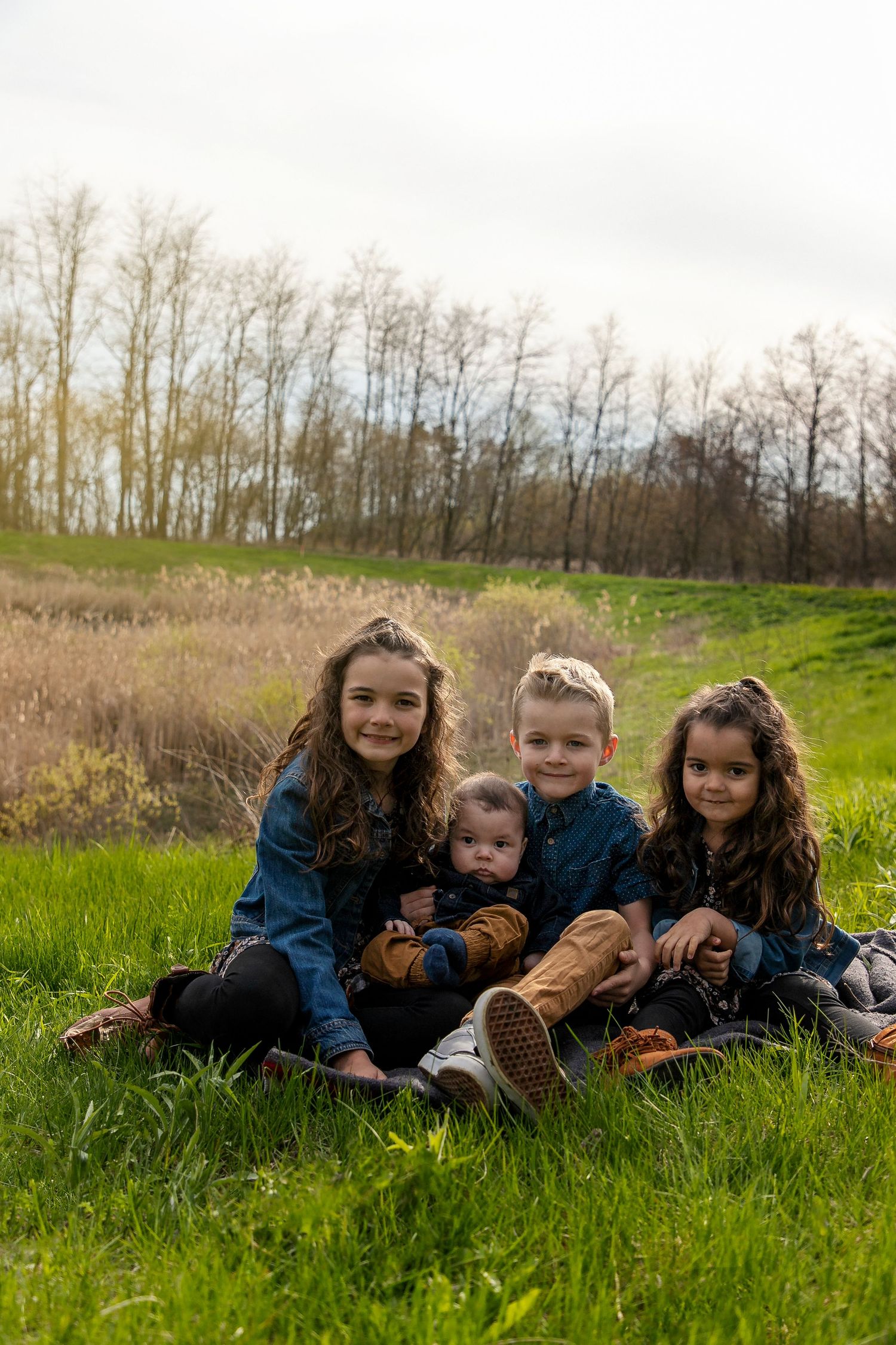 4 kids sitting on a blanket in a grassy field, smiling.