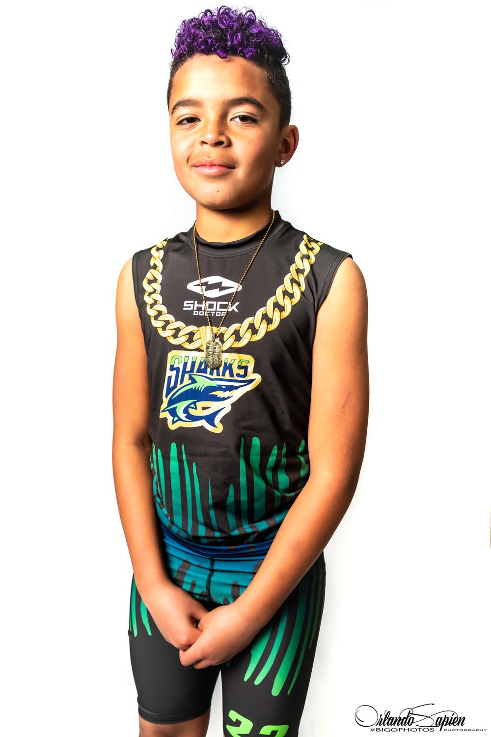 Young person wearing a black and teal basketball jersey with a gold chain necklace posing for photos.