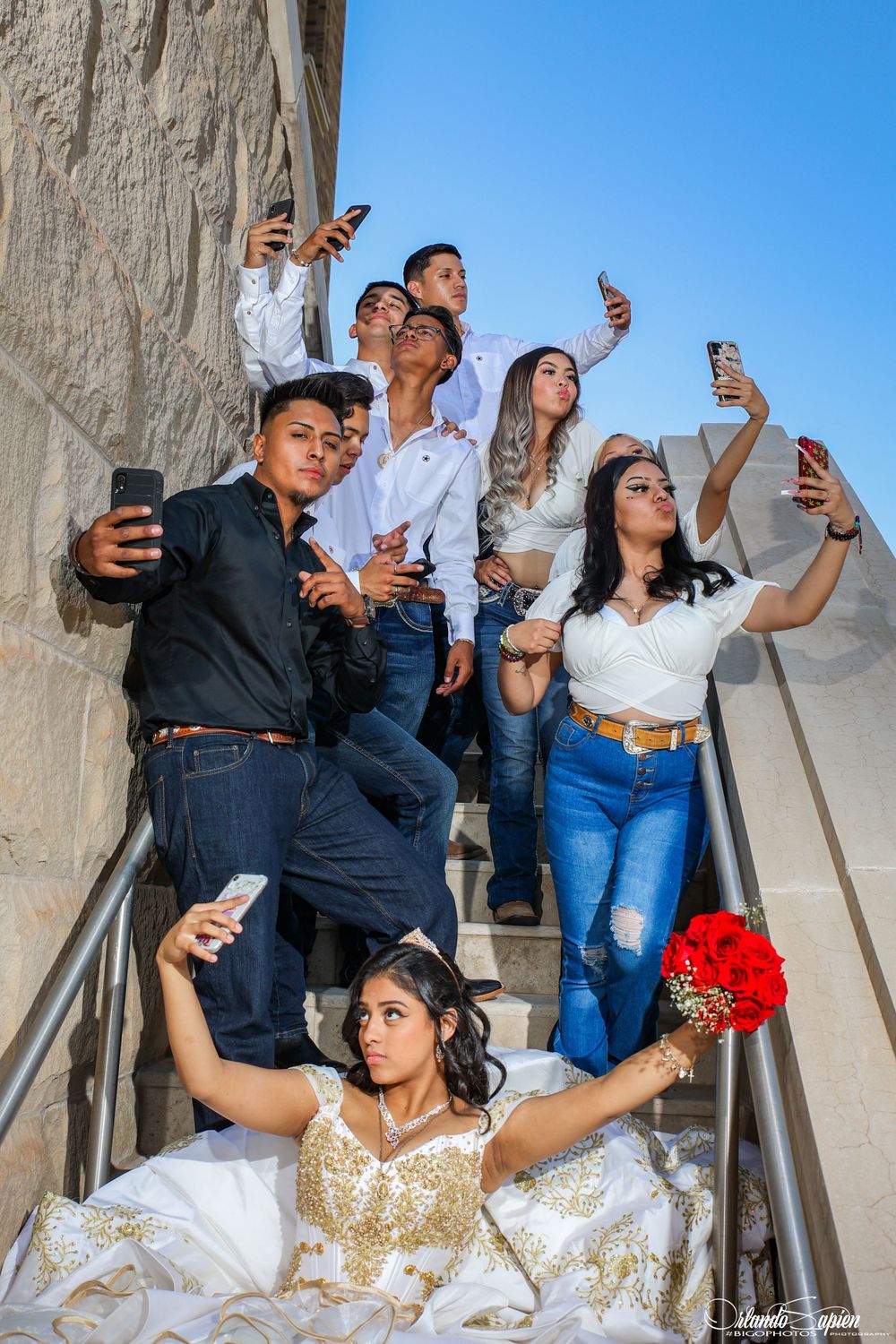 Group taking selfies and posing on concrete steps during formal event.