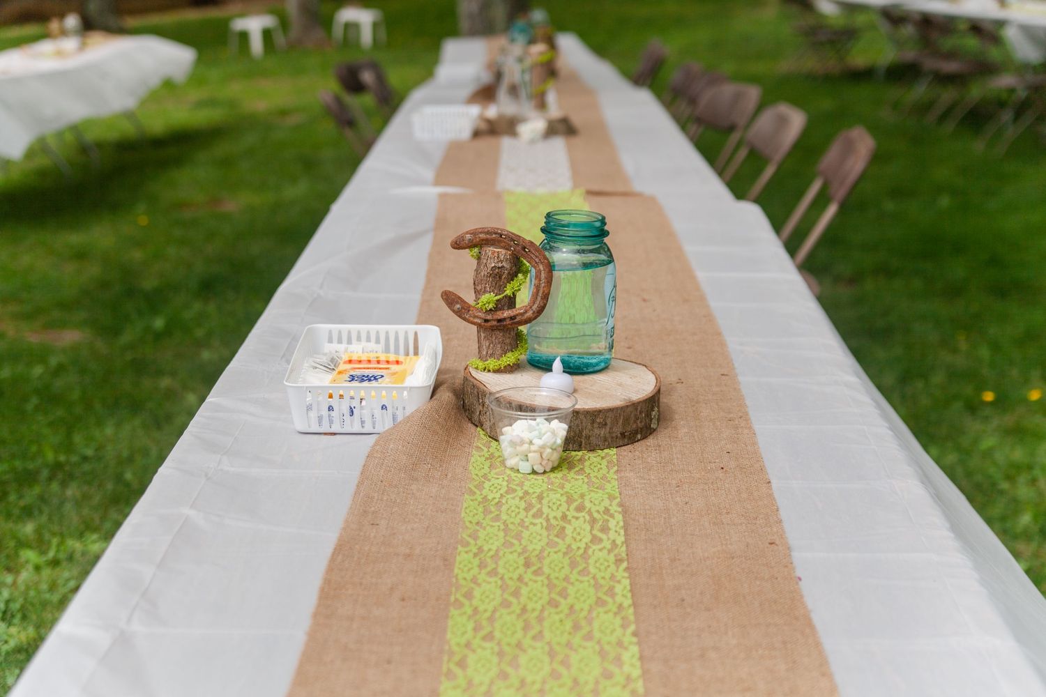 Outdoor wedding reception table setup with burlap runner and rustic decor.