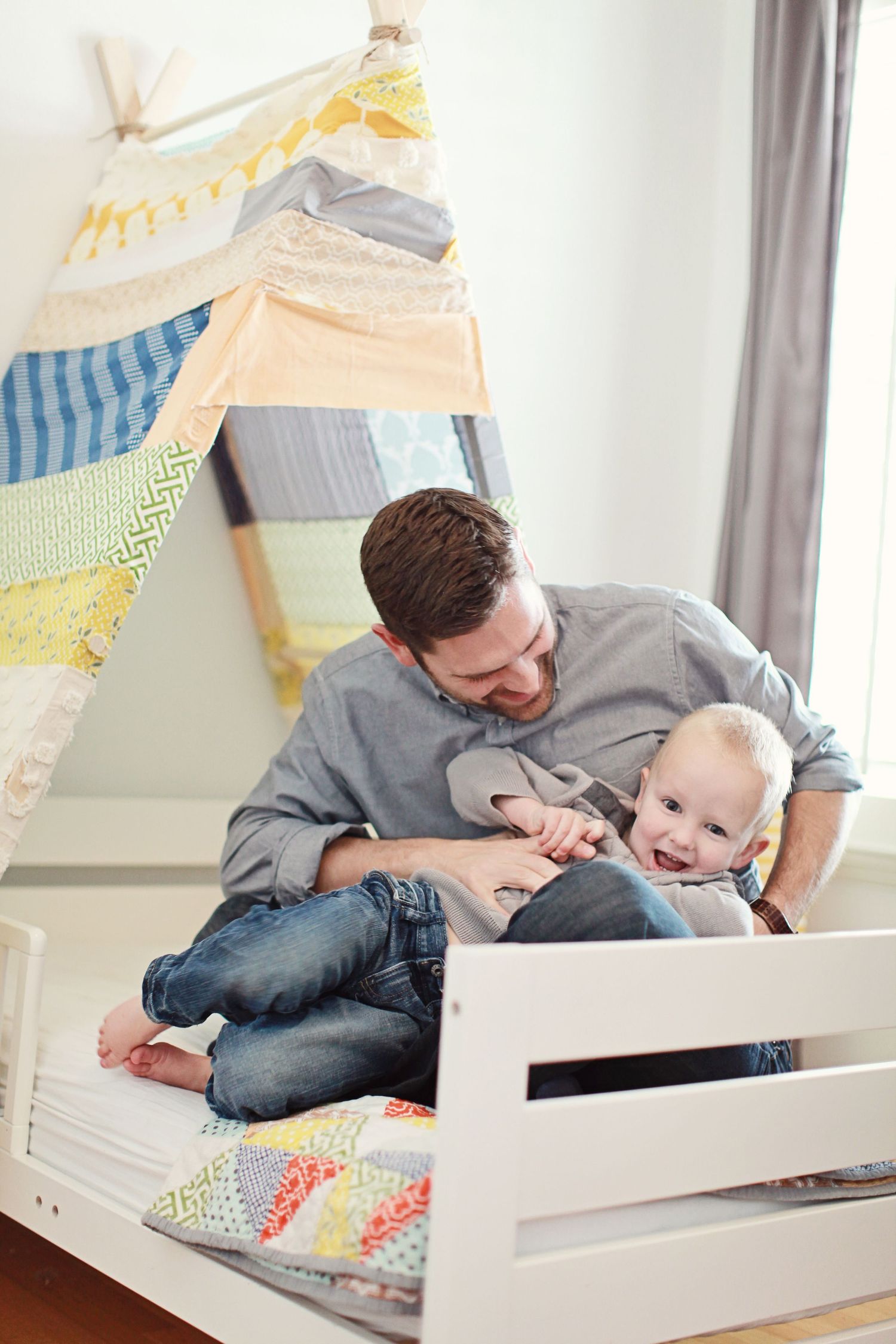 Parent and baby sharing playful moment on bed with colorful tent in background.