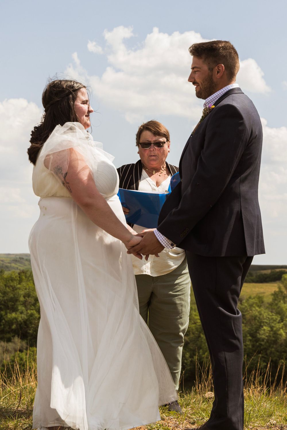 Wedding couple exchanging vows during hilltop ceremony with officiant present.