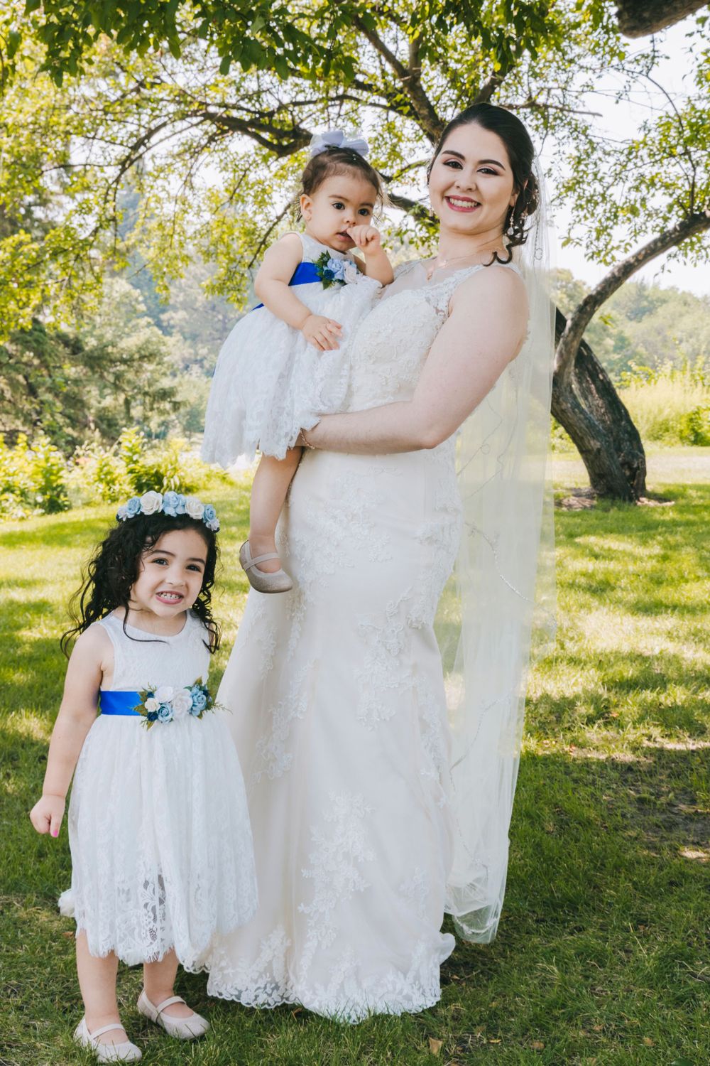 Wedding party members in white dresses with blue accents pose outdoors.