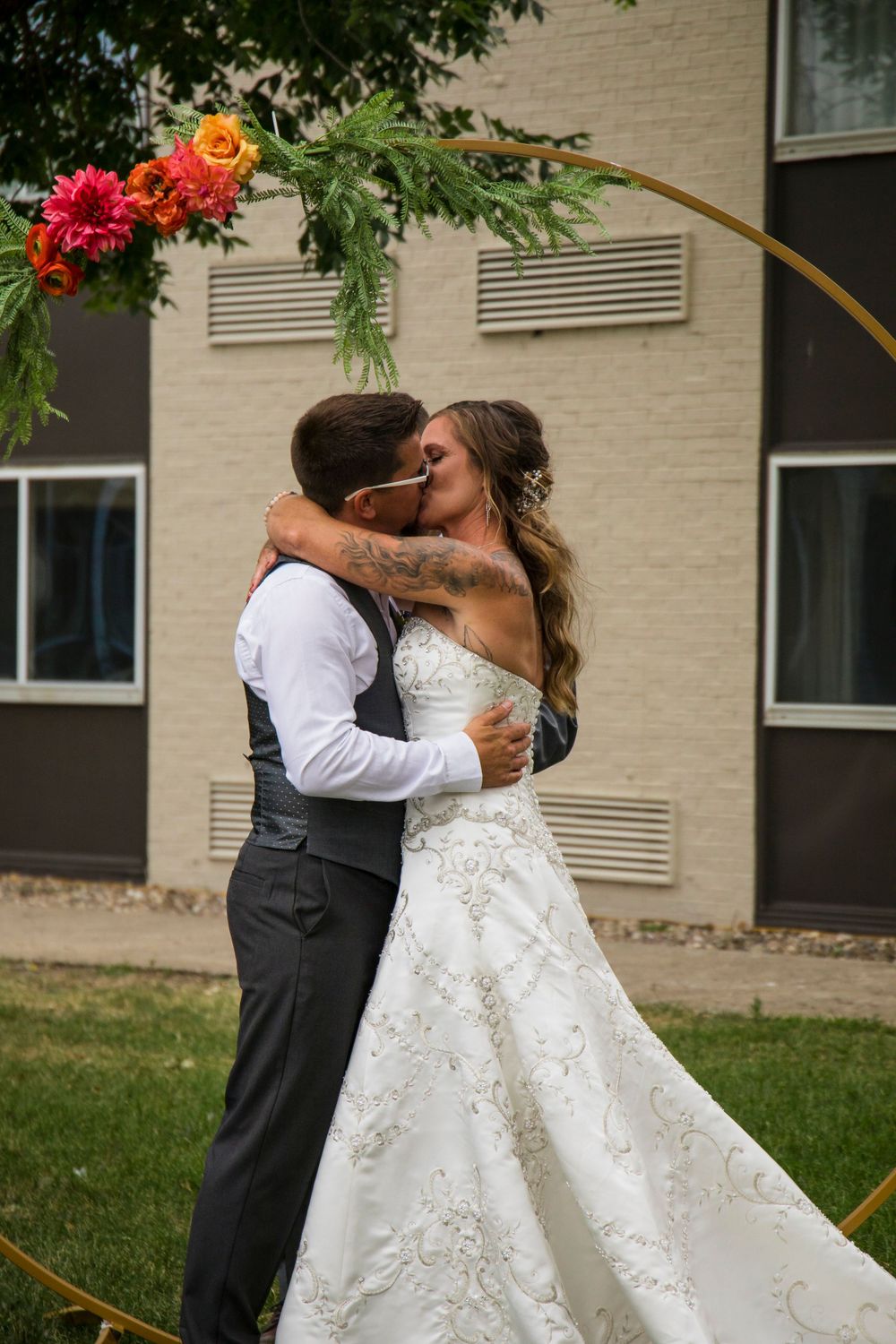 Intimate wedding moment captured under floral-decorated circular arch in garden setting.