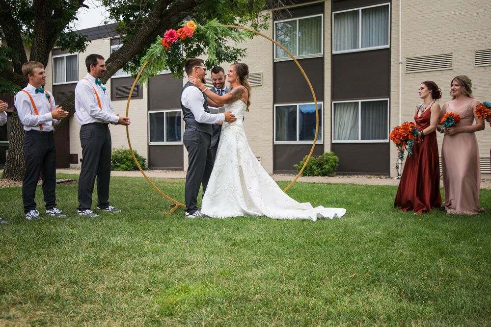 Outdoor wedding ceremony with gold hoop arch and bridal party in casual attire.