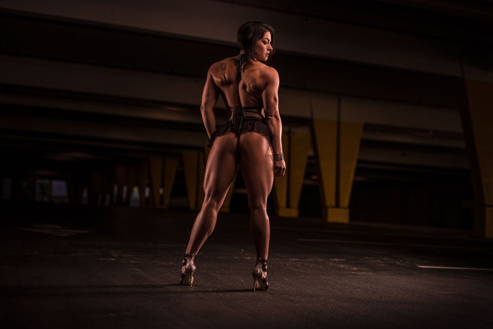 Athletic silhouette in dramatic lighting shows muscular form in urban parking structure.