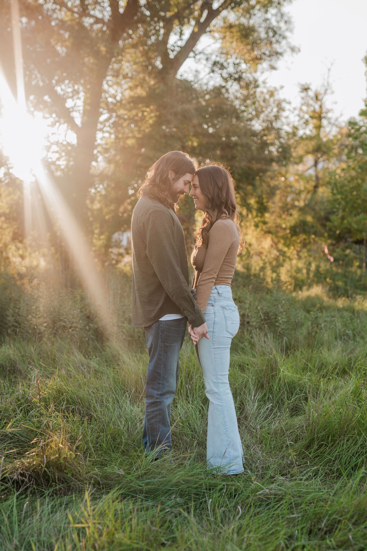 A couple stands close together in a sunlit field during golden hour.
