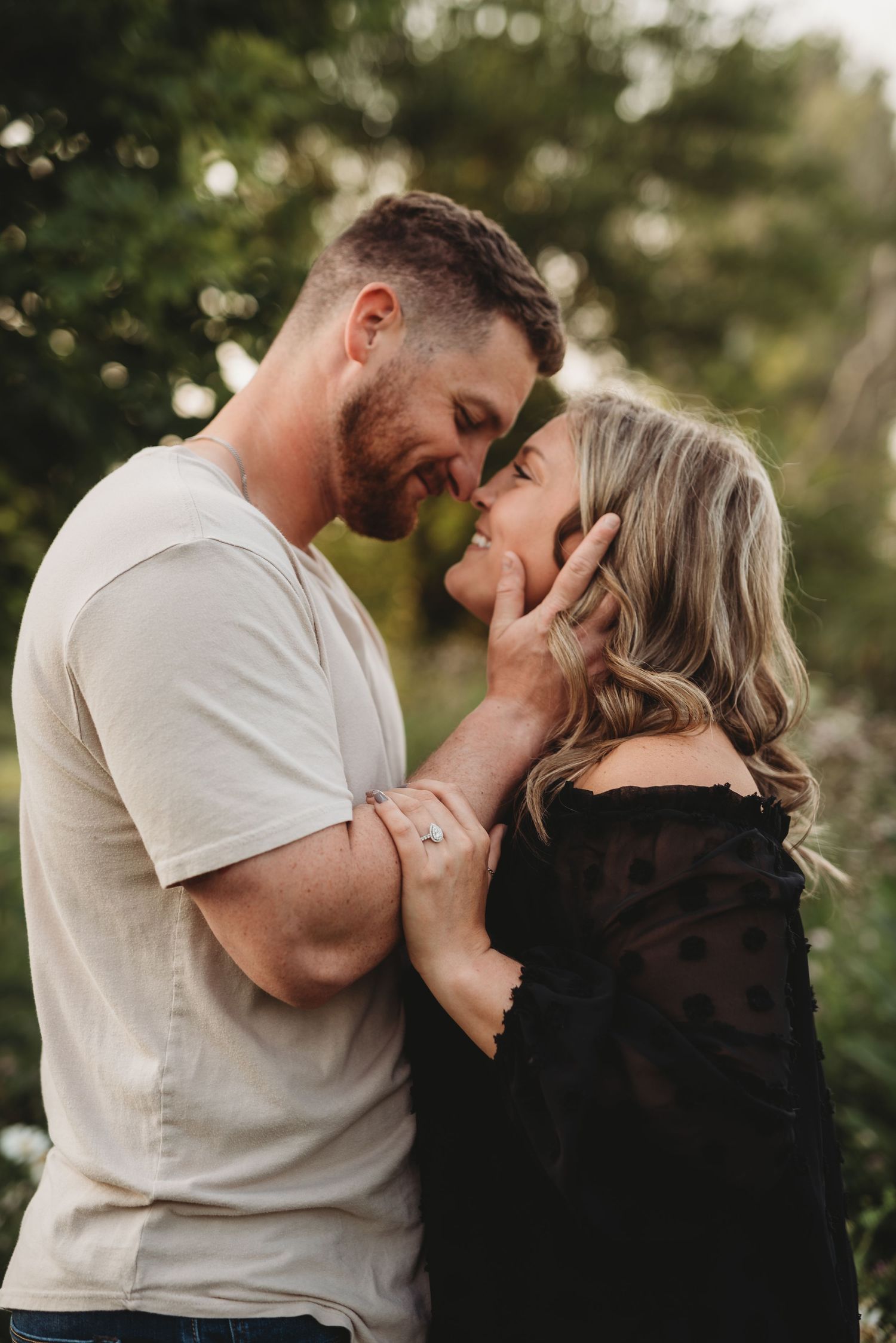 A romantic couple shares an intimate moment outdoors surrounded by green foliage.