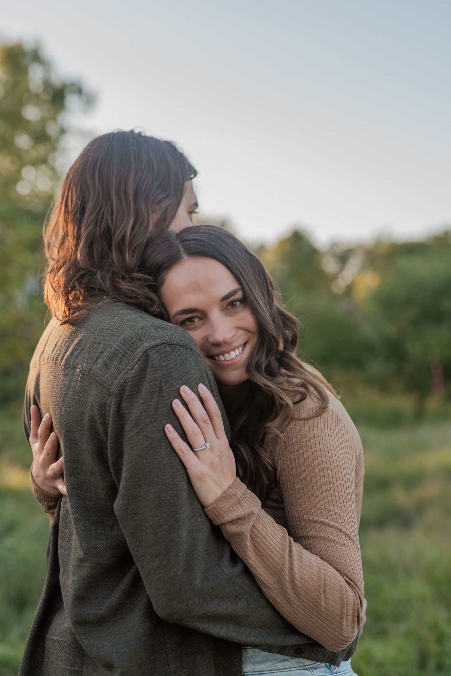 Two people share an affectionate embrace in a sunny outdoor setting.