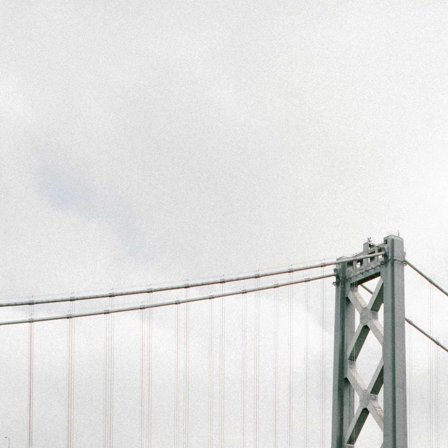 Minimalist view of Bay Bridge support tower against cloudy sky.