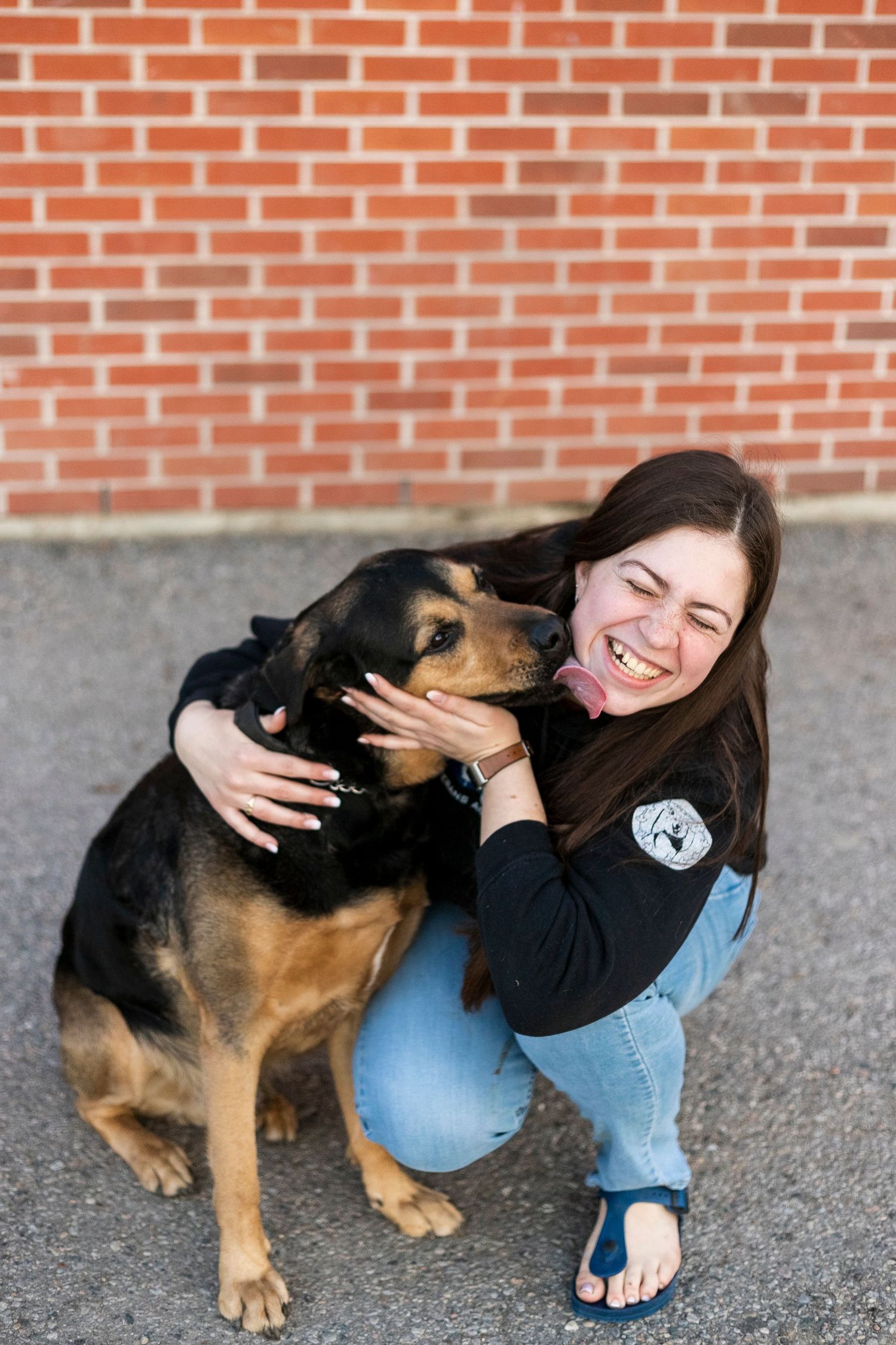 a Rottweiler, german shepherd mix dog sitting and happily licking or kissing a girl who is kneeling next to him
