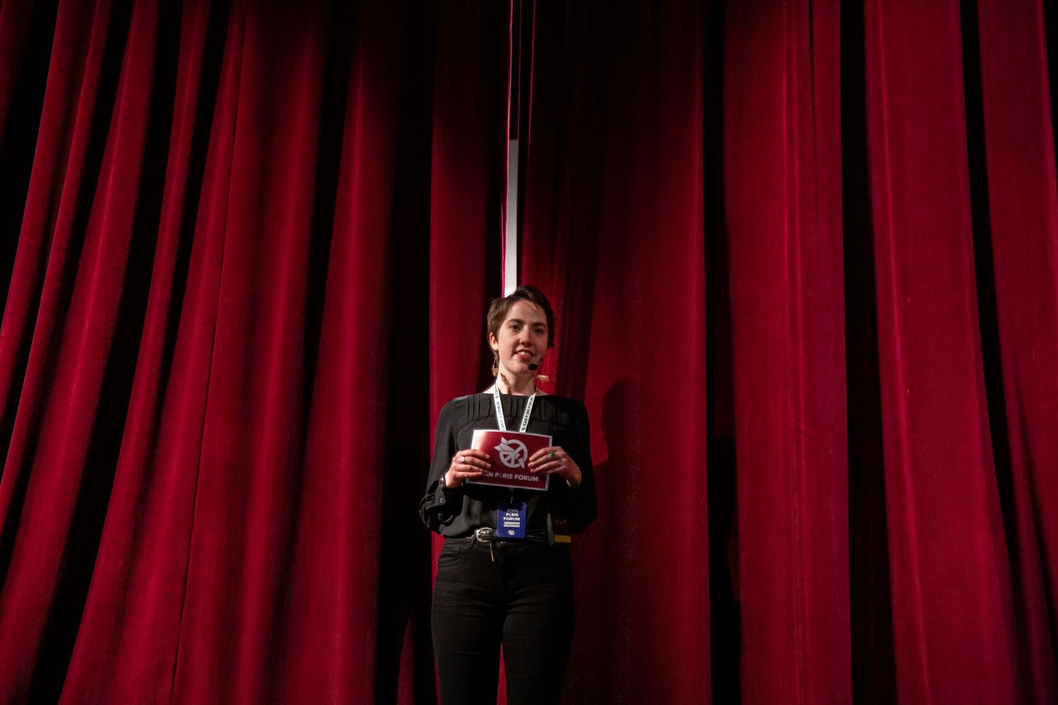 Speaker presenting on stage against red curtain backdrop at ICAN event.