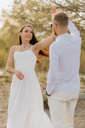 Couple in white attire dancing together outdoors against a soft natural backdrop.