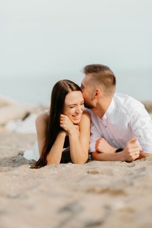 Romantic couple lying on sandy beach and sharing an intimate moment at sunset.