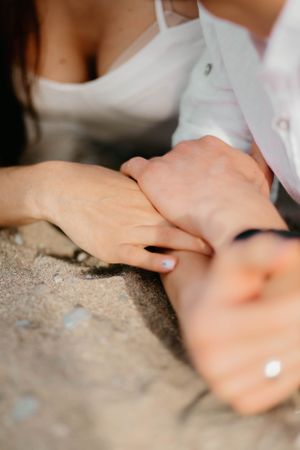 Close-up of hands touching tenderly on rocky surface with white clothing details.