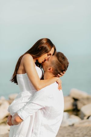 Tender moment between couple in white clothing by the ocean.