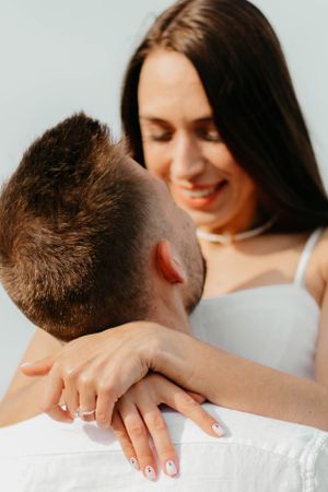 Close-up shot showing engagement ring while couple embraces in white outfits.