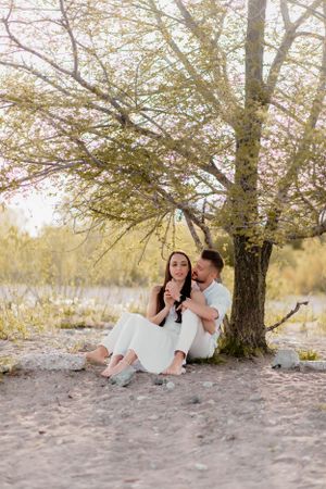 Couple in white clothing sitting together under blossoming tree.
