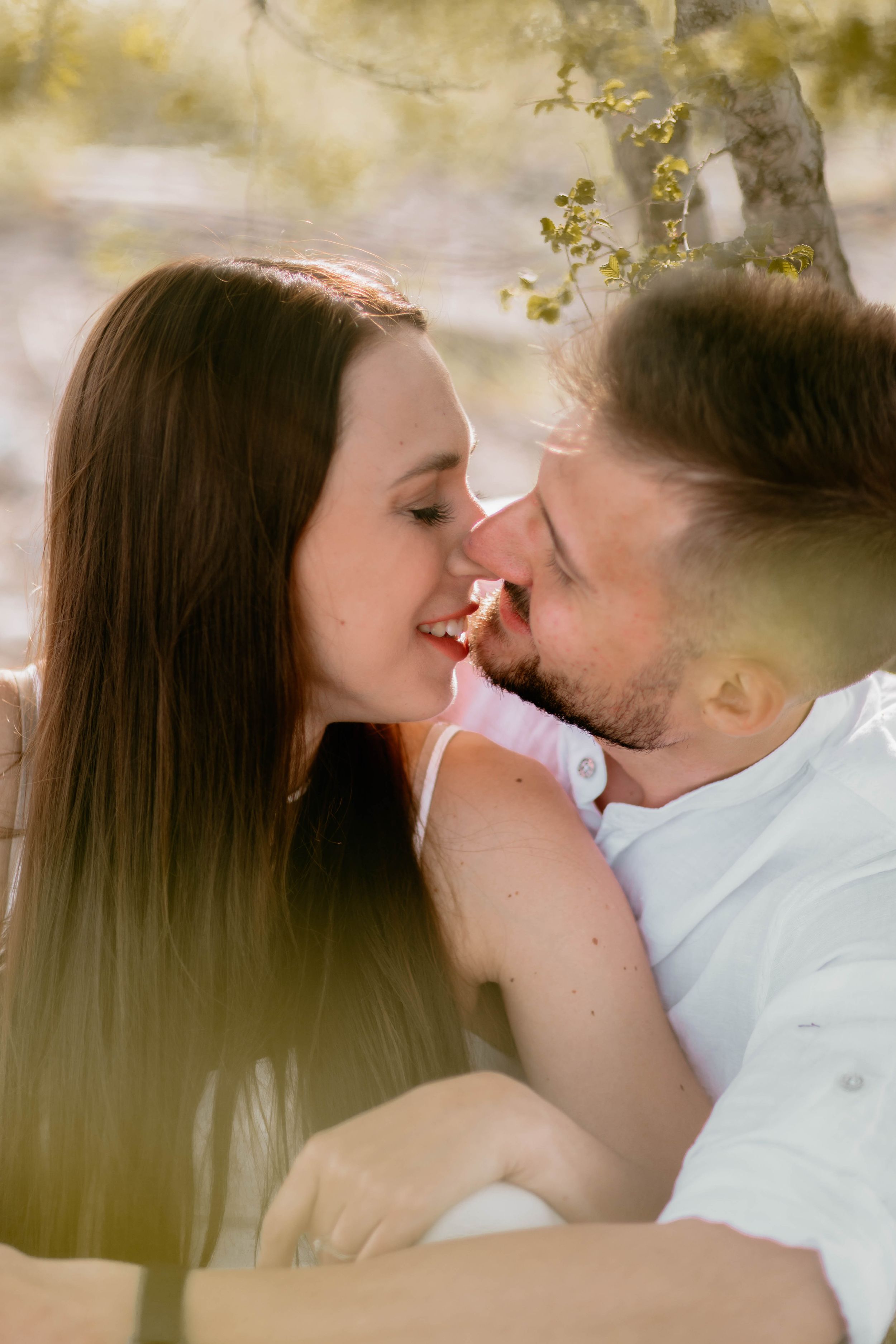 Romantic couple sharing tender moment under blooming tree branches.