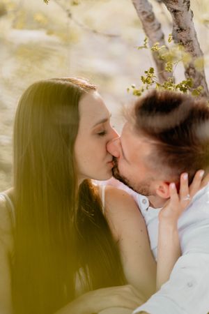Intimate kiss captured through spring tree branches in romantic setting.
