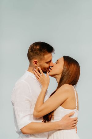 Romantic couple in white clothing sharing an intimate kiss against a light background.