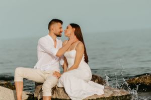 Romantic couple sharing tender moment while sitting on coastal rocks by the ocean.