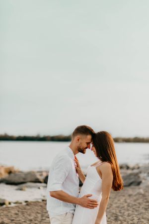 Intimate moment between couple dressed in white against coastal background.