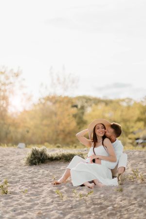 Couple in white clothing sharing romantic moment on sandy beach at sunset.