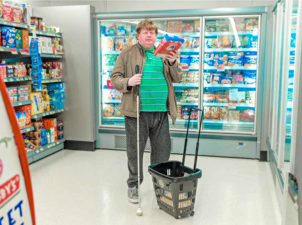 Person shopping with a basket in a grocery store freezer aisle.