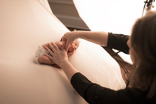 Laura, owner of Hope Believe Photography, posing a newborn baby boy on a tan blanket.