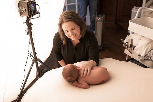 Laura, owner of Hope Believe Photography, looking down and smiling at a posed newborn baby boy.