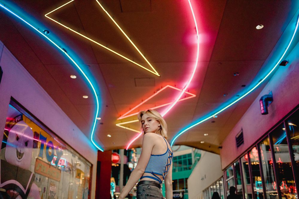 A neon-lit ceiling with colorful geometric patterns creates a vibrant atmosphere in a shopping mall interior.