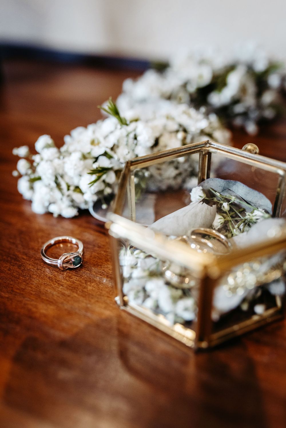 Wedding ring and floral decorations with gold hexagonal box on wooden table.