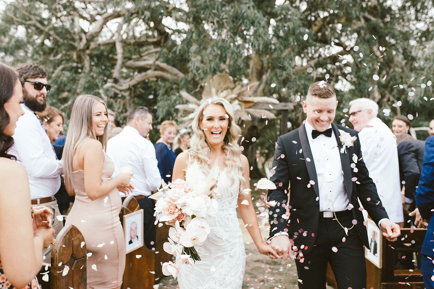 Wedding guests throwing white flower petals during outdoor celebration.