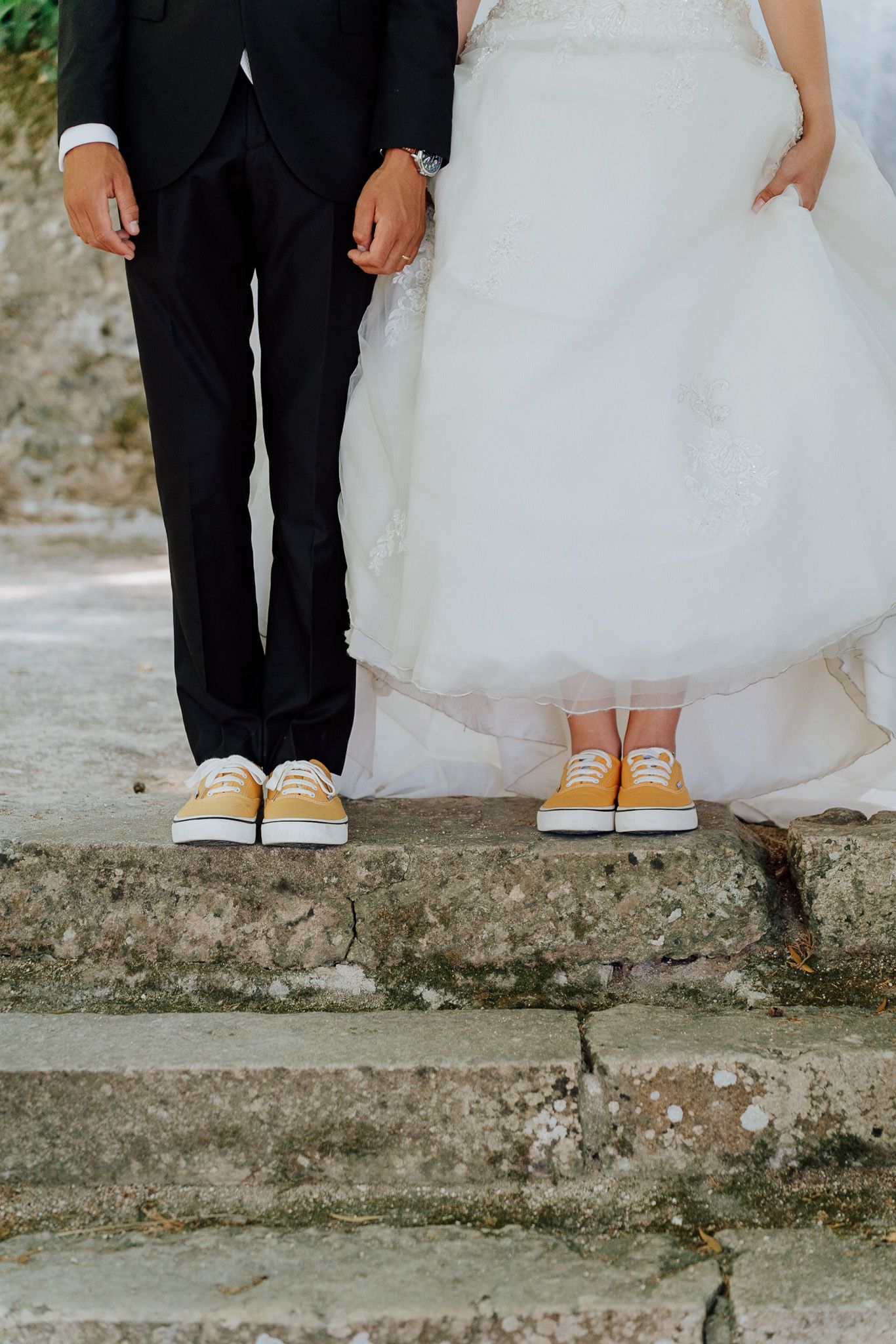 Wedding couple's feet wearing contrasting formal shoes and sneakers while standing on stone steps.