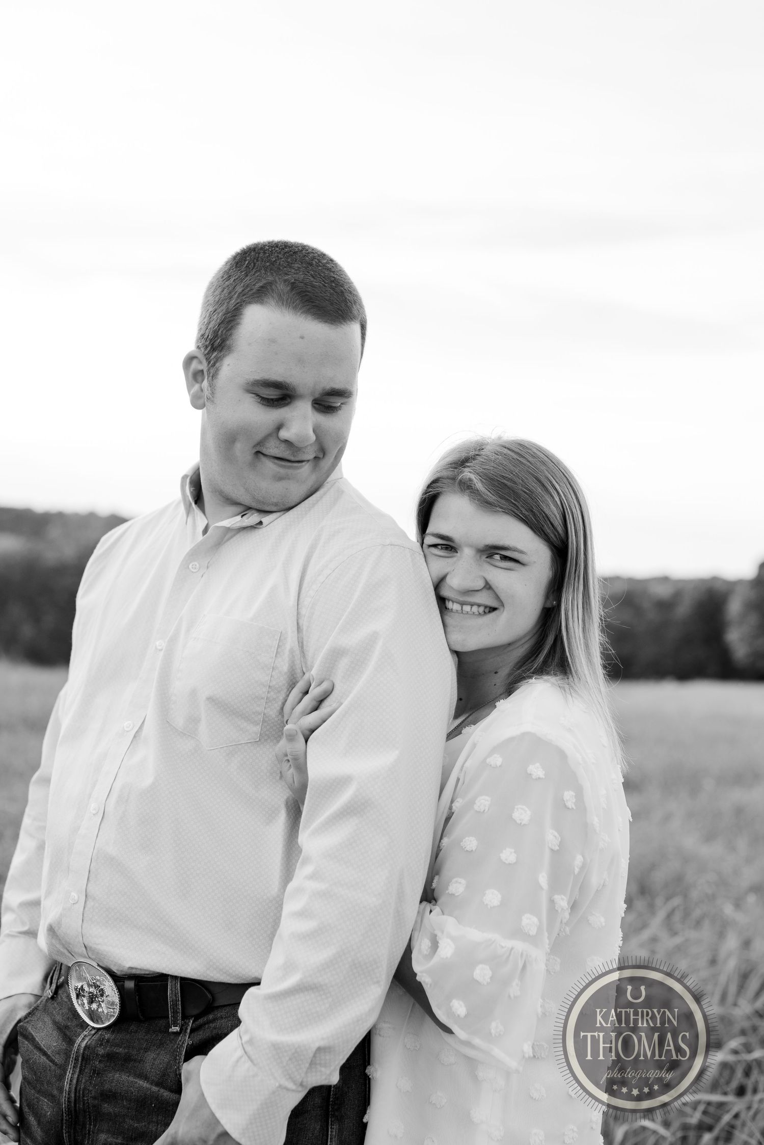 Black and white portrait of couple smiling together in outdoor field setting.