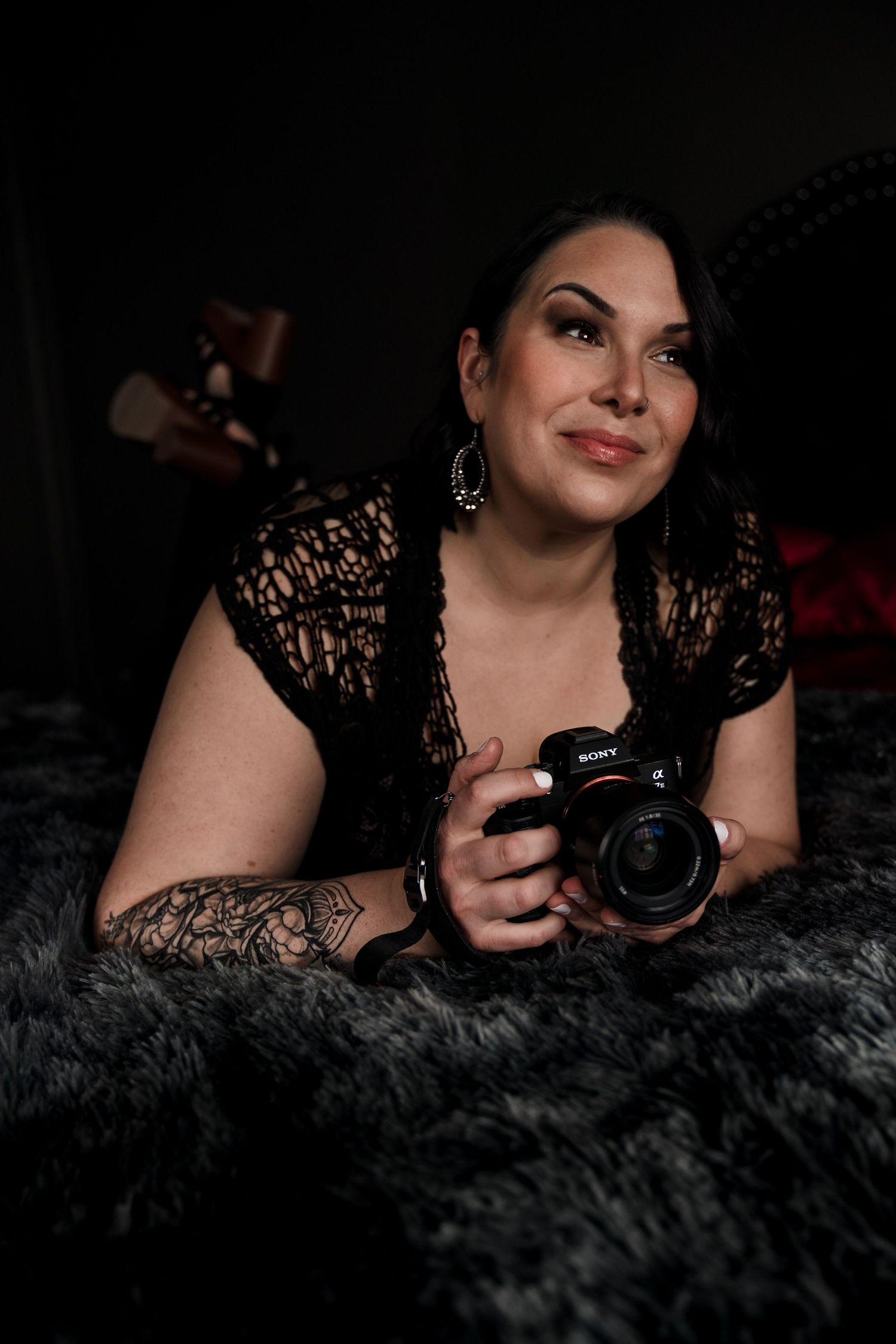 A glamour portrait session showing a person with a camera lying on dark fur fabric.
