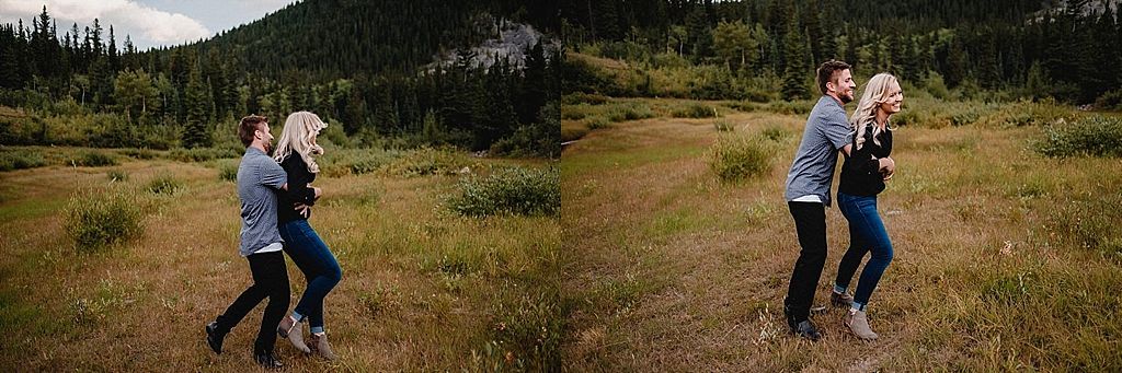 Playful couple dancing together in a mountain meadow with trees in background.